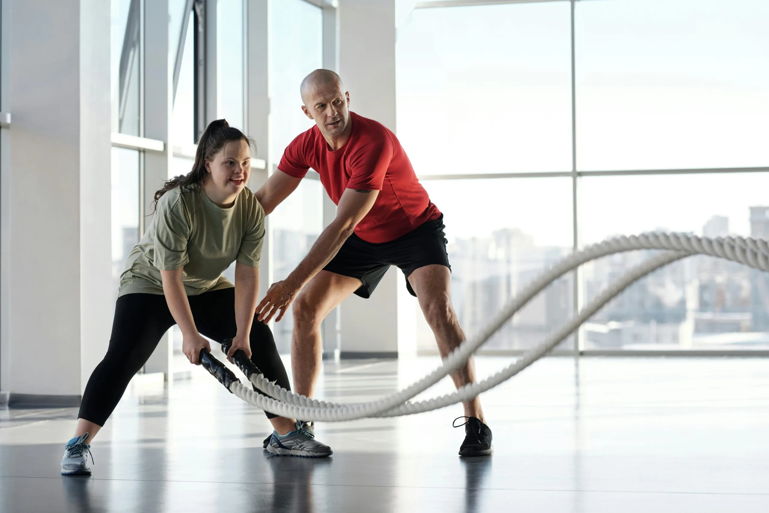 Woman and trainer engaging in rope workout in a bright gym, showcasing inclusivity and fitness motivation.