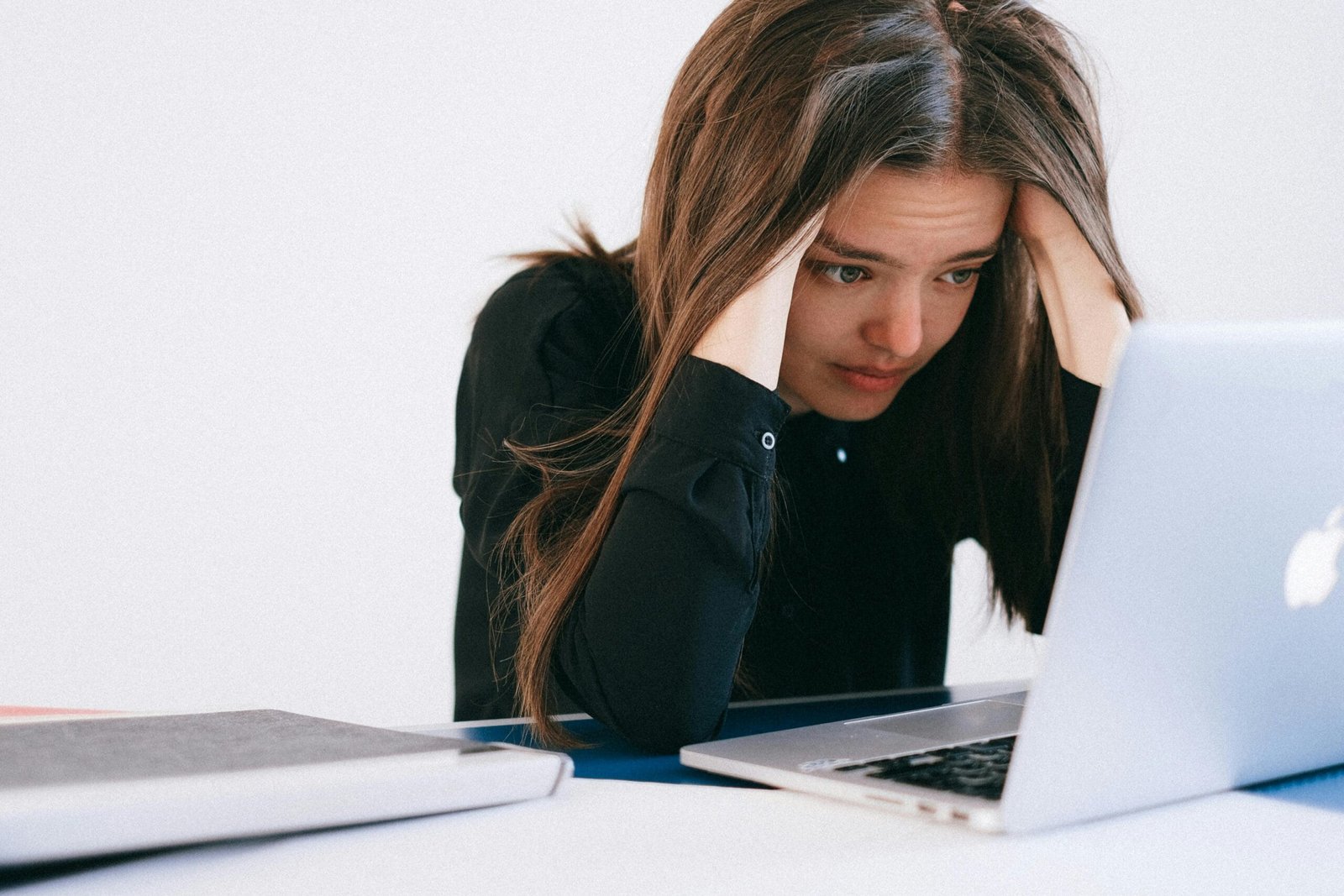 A stressed woman at a desk, looking at a laptop with a worried expression.