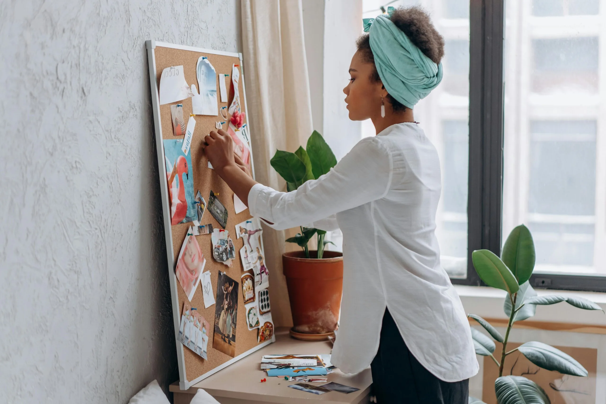 Woman in white shirt arranging a vision board in a modern apartment.